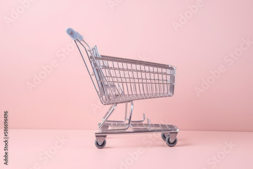 Caddie vide de supermarché à roulettes dans un fond de couleur uni rose