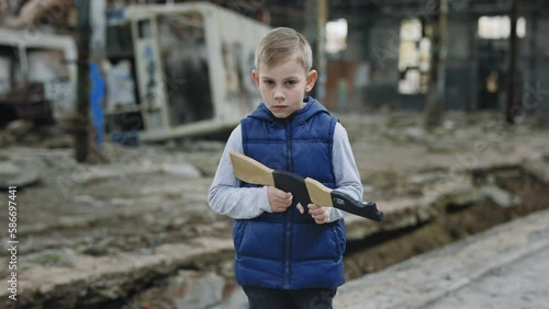 Portrait of the male child holds a toy gun against a background of devastation place. Boy games. War. Boy playing in water standing in the destroyed plant photo