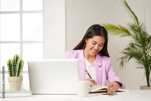 portrait of asian business woman in pink jacket working with computer and notebook in office
