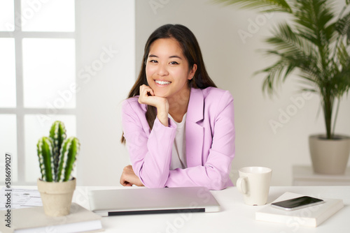 portrait of asian business woman resting her hand on her chin and looking at camera in office © Retamosa