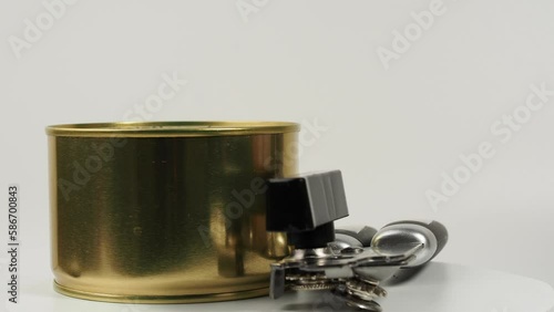 A can opener with a tin can rotates on a white background. Metal can opener. Close-up.
