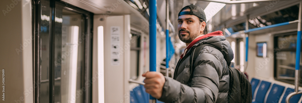 A young man rides standing in a modern subway car.