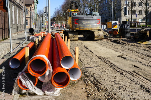 Street reconstruction site, stacked plastic sewage pipes, vertical well, excavator, dewatering pump