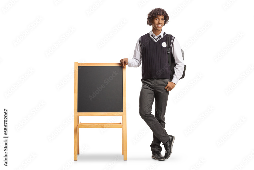 Full length portrait of a male african american student in a uniform leaning on blackboard Full length portrait of a male african american student in a uniform leaning on blackboard
