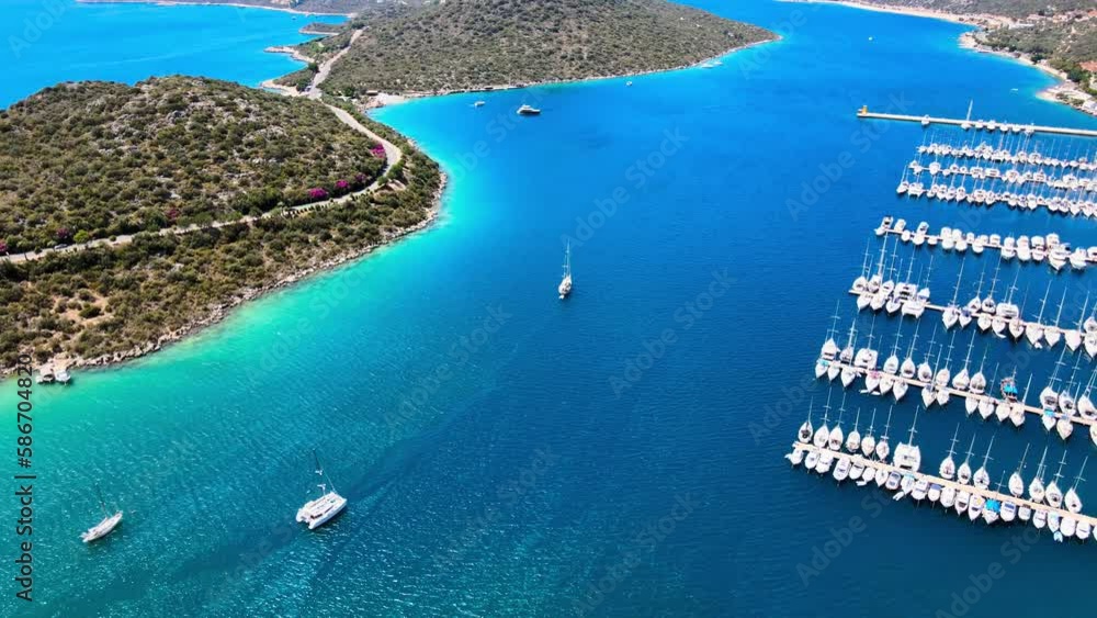 Stunning drone footage of yachts sailing in the beautiful marina of Kaş, Antalya, showcasing the breathtaking landscape, turquoise waters, and sandy beaches, making it an ideal vacation destination.