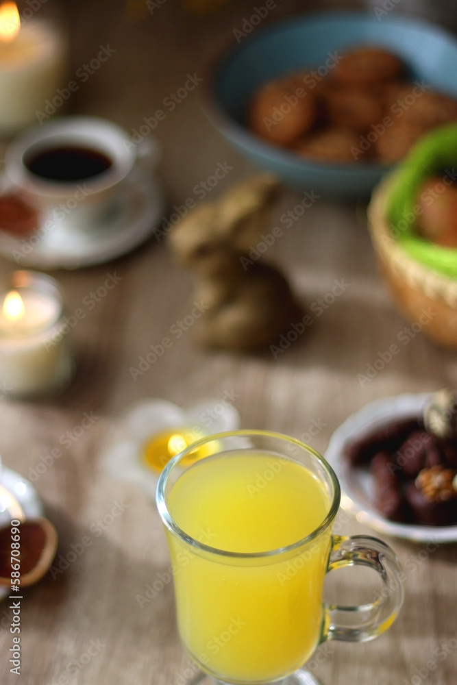 Easter eggs in the basket, bowl of cookies, chocolate pralines, Easter bunny figurine, cups of tea, glasses of juice, flowers and lit candles on the table. Selective focus. Easter eggs in the basket, bowl of cookies, chocolate pralines, Easter bunny figurine, cups of tea, glasses of juice, flowers and lit candles on the table. Selective focus.