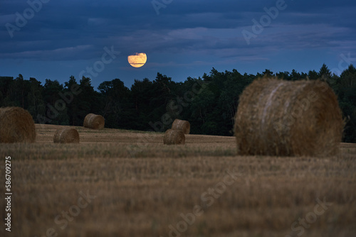 Full moon over forest field with bales of straw