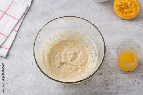 Glass bowl with egg-butter mixture, freshly squeezed orange juice on a gray background. Cooking greek easter  cookies koulourakia step by step instruction. Do it yourself. Step 3. Add orange juice