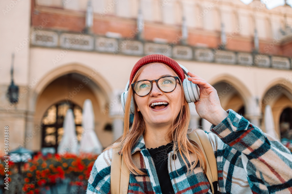 Fototapeta premium Young blonde woman smiling happy using smartphone and headphones, posing in street of European Krakow city. High quality photo