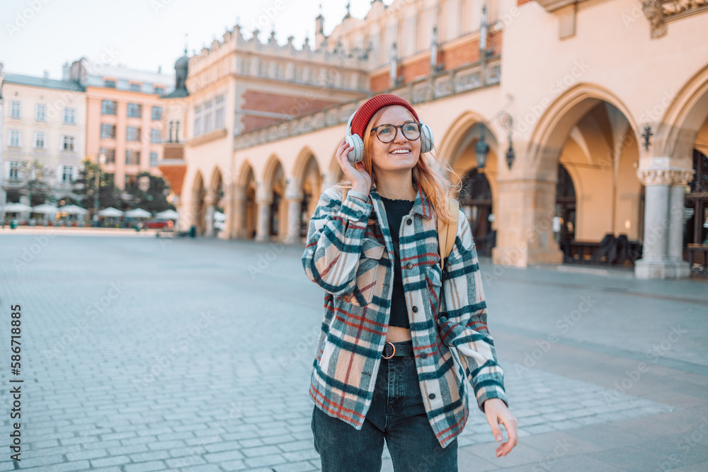 Young blonde woman smiling happy using smartphone and headphones, posing in street of European Krakow city. High quality photo