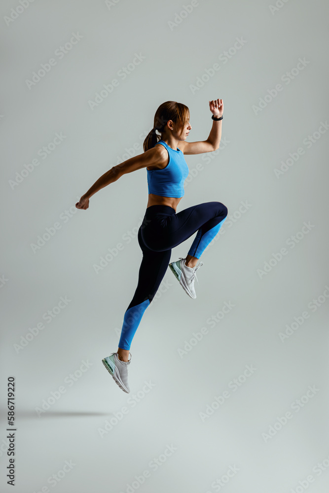 Woman running in Mid-Air exercising during cardio workout over studio background. High quality photo