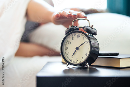 Woman on the bed reaches her hand to turn off the alarm clock