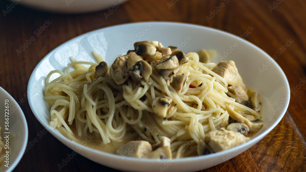 Spaghetti on a plate. Cooked spaghetti on a plate with mushrooms. White plate on a wooden table Spaghetti on a plate. Cooked spaghetti on a plate with mushrooms. White plate on a wooden table