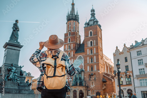 Back view of traveller woman walking on old Market Square in Krakow holding tourist map. Travel and active lifestyle concept. High quality photo