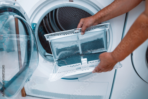 Horizontal photo of female hand taking the lint out from dirty air filter of the dyer machine 
