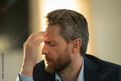 Stressed business man having headache at home office. Tired businessman is working overtime and has headache. Portrait of senior suffers from headache. Migraine from overwork, difficult at work.