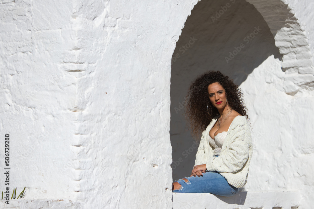 latin woman with dark curly hair and middle age is sitting on a wall. The woman is sad and pensive. The woman is a single mother.