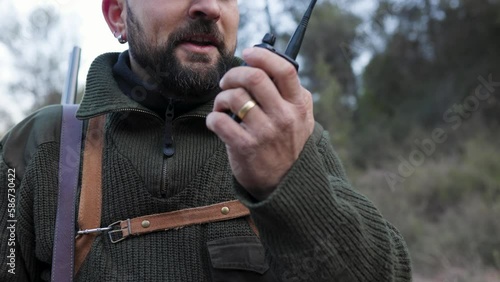 Close up view of a hunter man talking to someone on a walkie talkie outdoors.