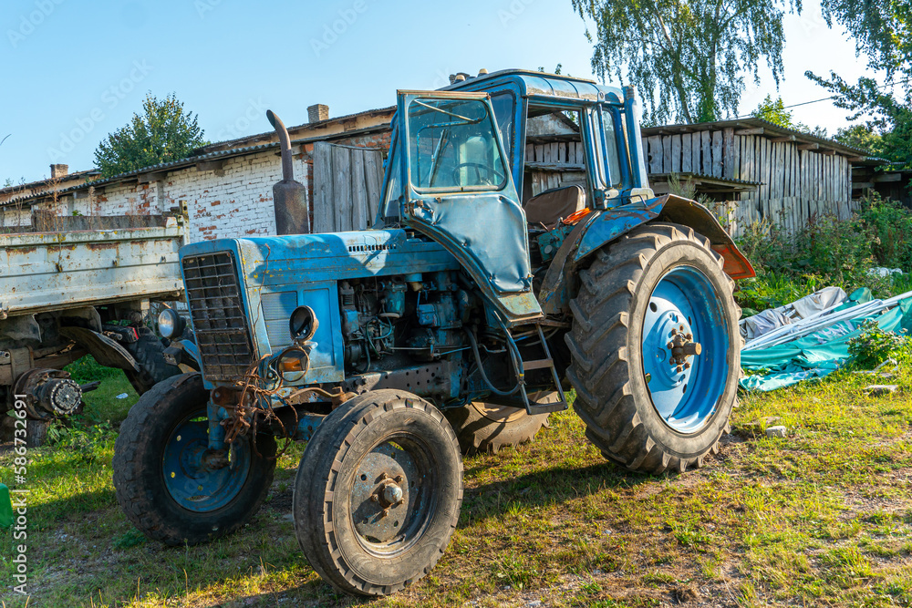 Fototapeta premium An old rusty Soviet-era tractor is parked on a farm plot. Repair of agricultural machinery. Poor regions of Russia. Lack of financing of private farms.