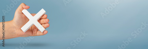 White multiplication symbol or cross in hand. The concept of prohibition or removal. Mathematical white symbol multiply in hand on a blue background