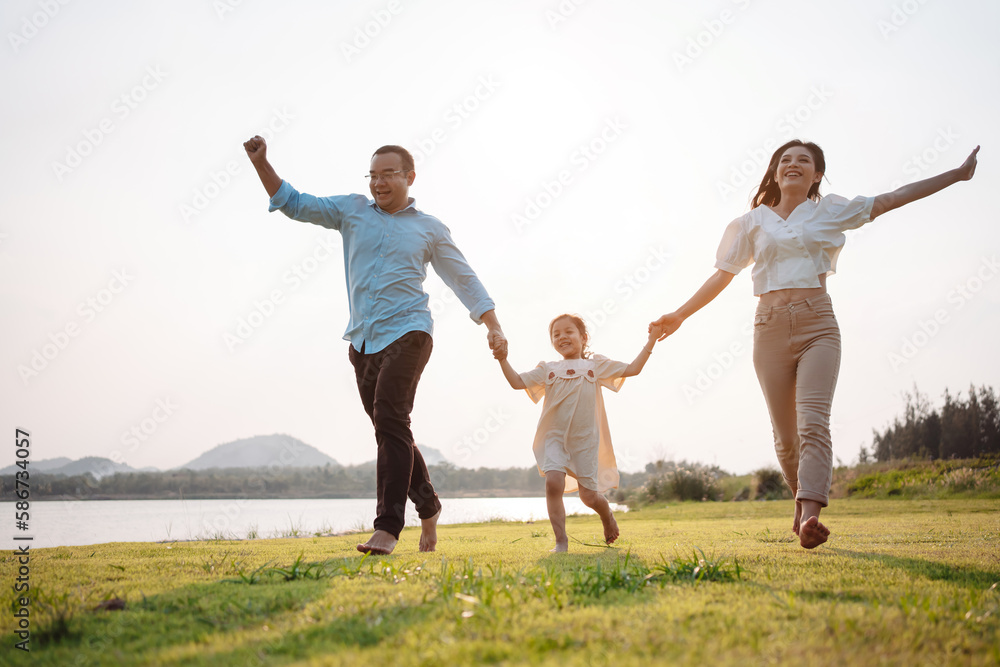 Happy family in the park sunset light. family on weekend running together in the meadow with river Parents hold the child hands.health life insurance plan concept. Happy family in the park sunset light. family on weekend running together in the meadow with river Parents hold the child hands.health life insurance plan concept.