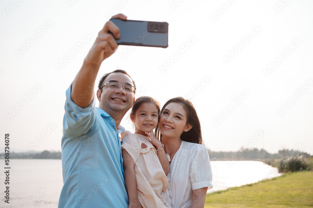 Happy family in the park on weekend. family enjoying together in the meadow with river Parents hold the daughter.health life insurance plan concept. Happy family in the park on weekend. family enjoying together in the meadow with river Parents hold the daughter.health life insurance plan concept.