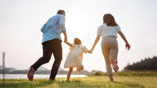Happy family in the park sunset light. family on weekend running together in the meadow with river Parents hold the child hands.health life insurance plan concept.