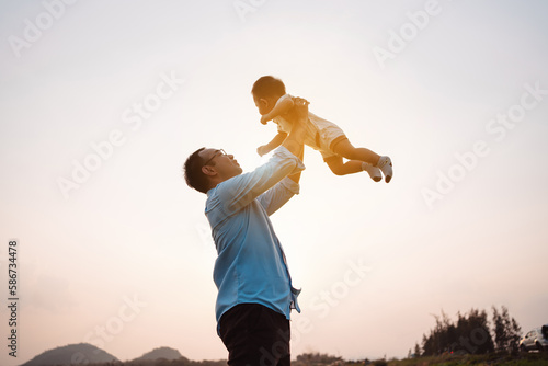 Fatherhood lifting baby son enjoying in the park near river at sunset.