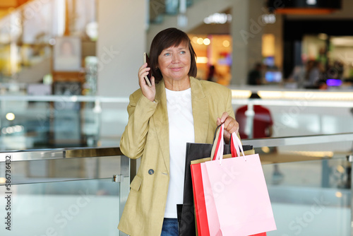 Stylish adult woman blogger with shopping bags and smartphone is communicating with followers in social networks near shopping mall. concept of consumerism, sale, rich life, virtual life. Black Friday