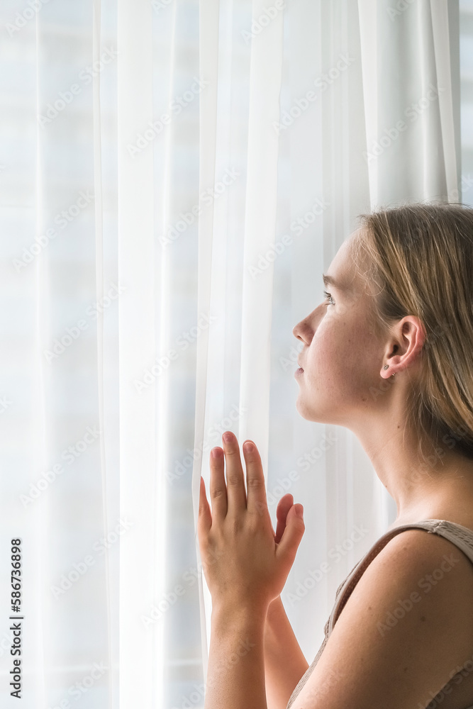 Concentrated beautiful girl sits and looks out the window at home. Woman sadly contemplatively looks out the window alone.. Concentrated beautiful girl sits and looks out the window at home. Woman sadly contemplatively looks out the window alone..