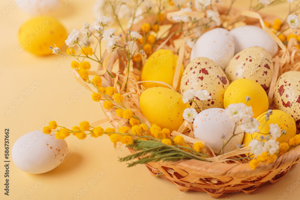 Obraz premium Easter candy chocolate eggs and almond sweets lying in a bird's nest decorated with flowers and feathers on a yellow background. Close up. Happy Easter concept.