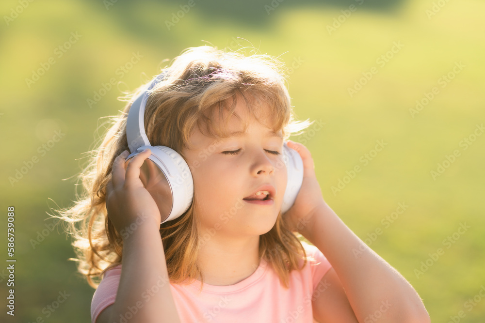 Singing children. Stylish teen boy listening music in headphones and singing against green grass summer background. Portrait of kid in headphones listening music with closed eyes.