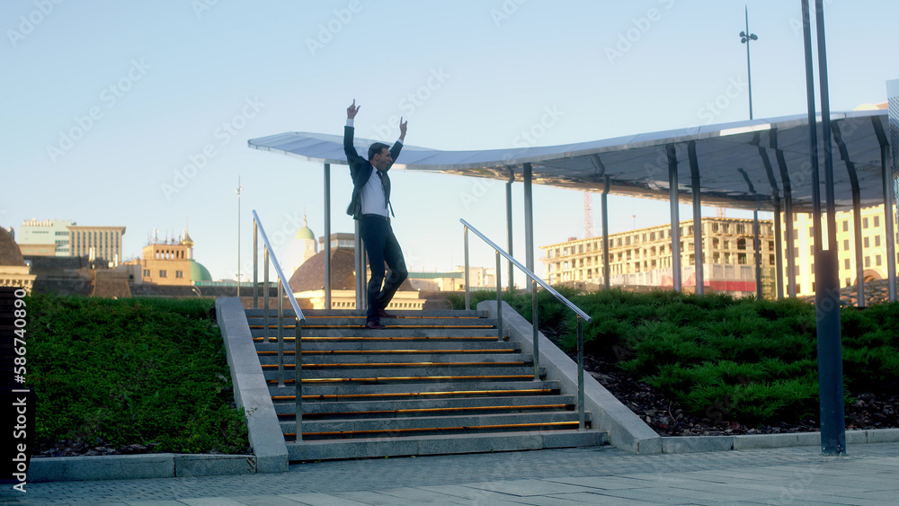 successful businessman in suit rejoices and fools around on stairs like joker. man dancing and raising his hands up, getting promotion at work, closing deal, exiting venture capital, getting money.