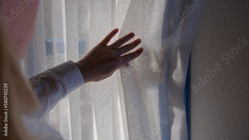 View over shoulder woman hand in white shirt open curtains and vintage old window blue color. retro handle on window of house in bedroom. concept of traveling to hotels in different countries.