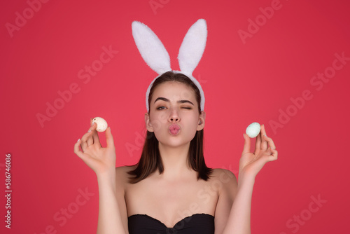 Cheerful young woman wearing Easter bunny ears holding decorative colored eggs on studio background with copy space.
