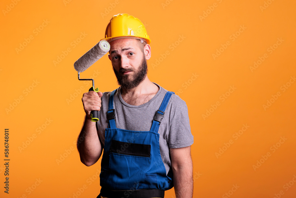 Professional painter working on renovation with roller, painting walls with color and paintbrush. Construction worker holding rolling brush to do diy renovating project over studio background.