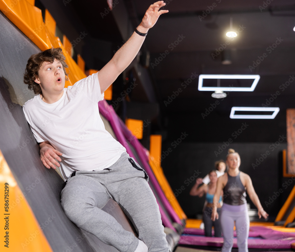 Smiling young guy in white t-shirt and gray sweatpants having great time  while jumping on trampoline in game club Stock Photo | Adobe Stock