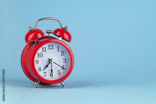 Red alarm clock on a light blue background. It's 7:30 o'clock on the clock. Morning. Place for text.