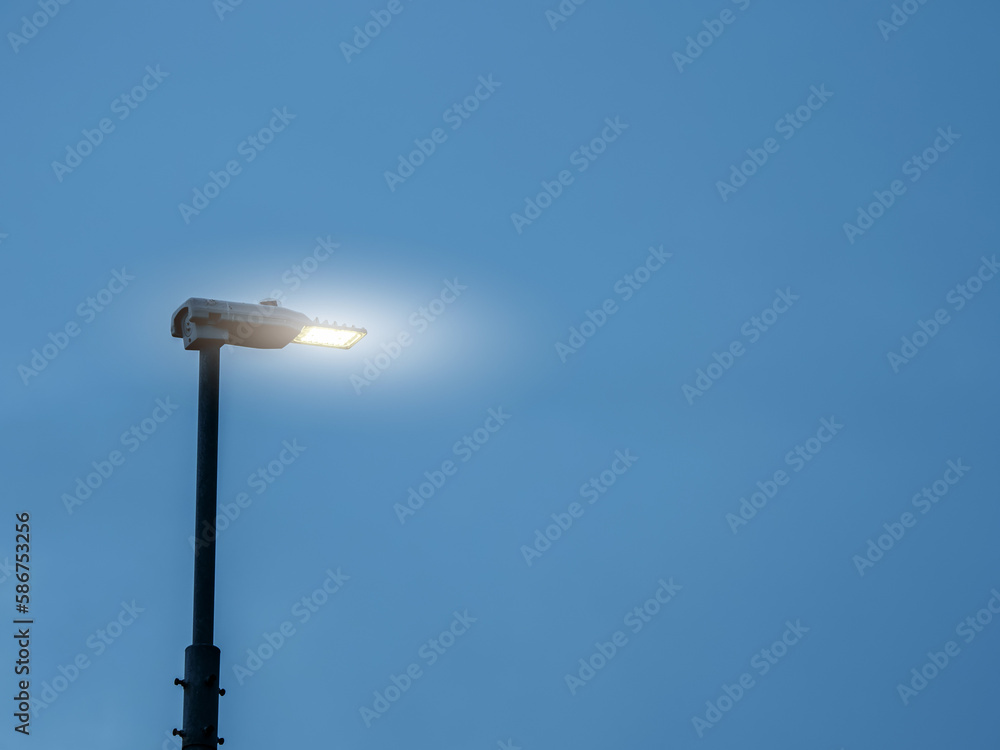 Modern LED energy saving lamp in a street on a metal pole against blue color sky. Illuminating streets concept. Technology and upgrade theme. Modern LED energy saving lamp in a street on a metal pole against blue color sky. Illuminating streets concept. Technology and upgrade theme.