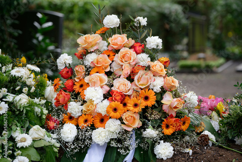 stylish funeral flowers of white carnations, orange gerbera and red and pink roses on a grave after a funeral