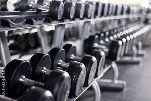 Rows of dumbbells for free weight training on rack in gym, closeup view with selective focus. Modern sports equipment for for beginners and professional athletes