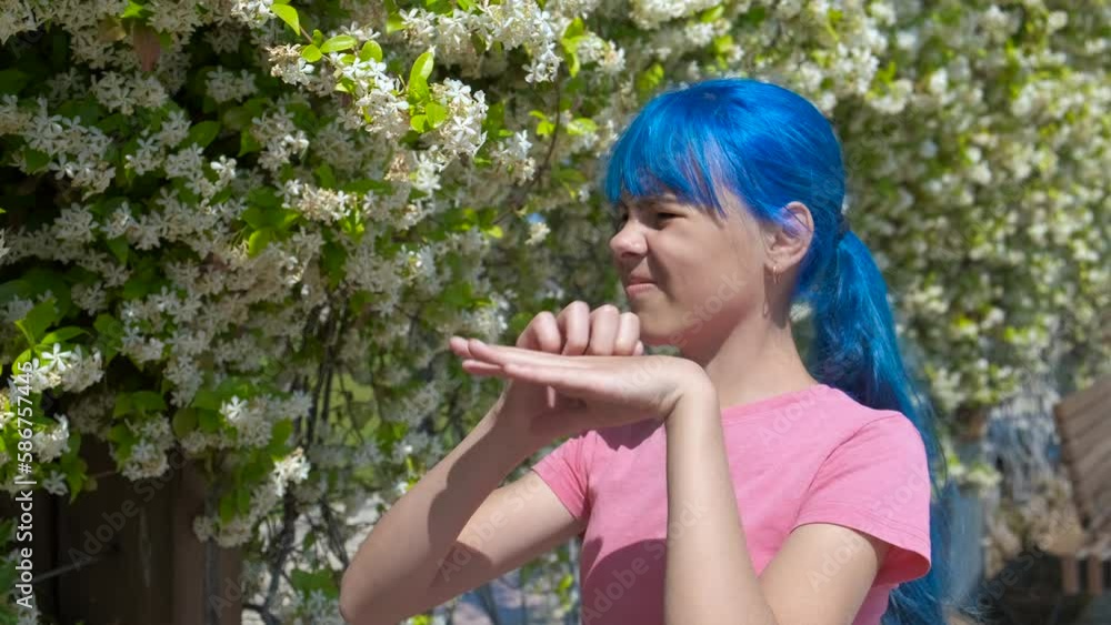 Itching on the skin of the hand. A teenager girl with blue hair smells flowers and scratches the skin of her hand. Itching on the skin of the hand. A teenager girl with blue hair smells flowers and scratches the skin of her hand.