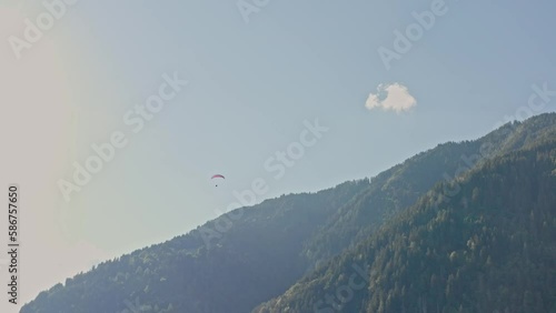 Bright red paraglider flies over large green valley and mountains. Picturesque view, located near the iconic Neuschwanstein castle, Germany, Allgäu region