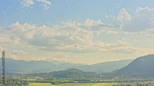 Bright red paraglider flies over large green valley and mountains. Picturesque view, located near the iconic Neuschwanstein castle, Germany, Allgäu region