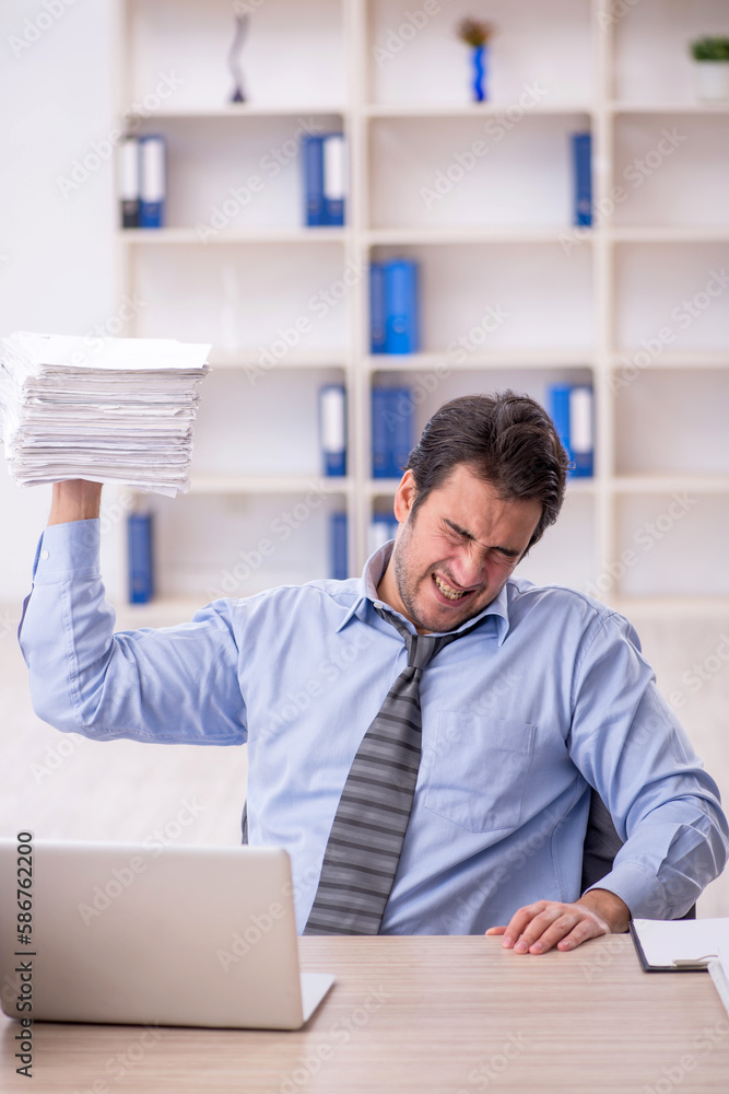 Young male employee and too much work at workplace Young male employee and too much work at workplace