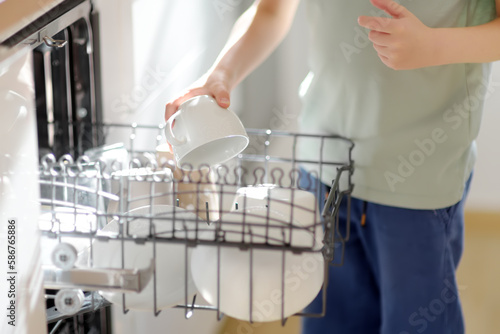 Obraz na plátně A preteen boy is loading dirty dishes into the dishwasher