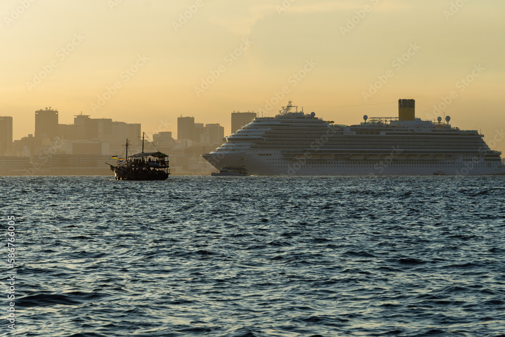 Transatlantic ship in Guanabara Bay in Rio de Janeiro, Brazil with a hill in the background. Beautiful landscape with the sea at sunset. Sailing boats and speedboats in the bay