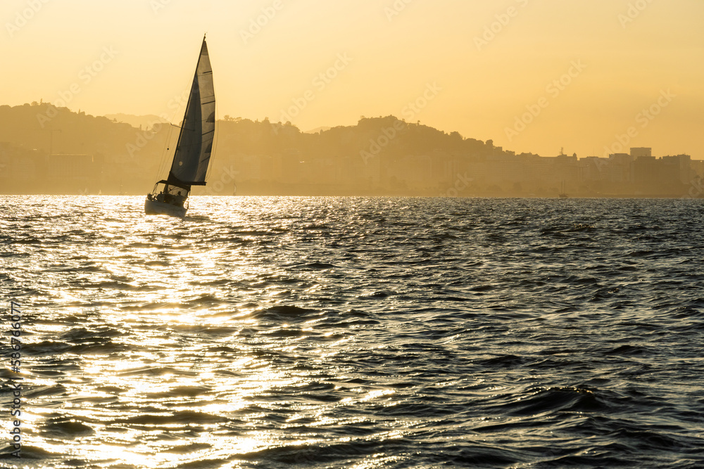 Sailing boat in Guanabara Bay in Rio de Janeiro, Brazil with a hill in the background. Beautiful landscape with the sea at sunset. Sailing boats and speedboats in the bay