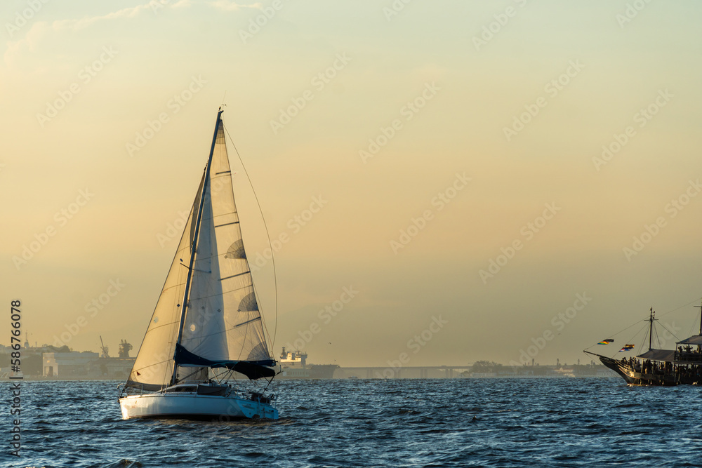 Sailing boat in Guanabara Bay in Rio de Janeiro, Brazil with a hill in the background. Beautiful landscape with the sea at sunset. Sailing boats and speedboats in the bay