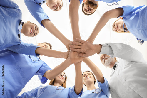 Doctor and interns stacking hands together against white background, bottom view